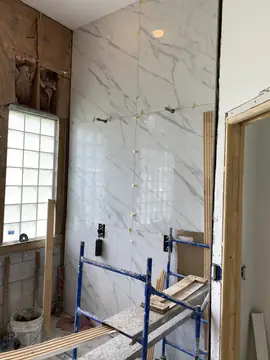 Pared de baño en gran formato con andamio. Revestimiento blanco con veta gris en piezas grandes durante la colocación, con niveladores y andamio delante.