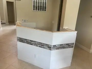 Frente de barra antes de la encimera. Barra revestida con pieza blanca en relieve y franja de mosaico, a la espera de colocar la encimera.