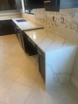 Encimera con faldón en tramo de escritorio. Encimera blanca con veta gris marcada y faldón hasta el suelo, con el frontal de la pared aún picado.