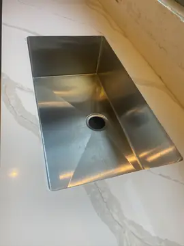 Fregadero bajo encimera veteada. Fregadero de acero bajo encimera blanca con veta gris, con la pared del frontal aún sin rematar.