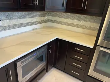 Encimera en L sobre muebles oscuros. Rincón de la bancada con encimera blanca de veta gris, cajones oscuros y frontal de mosaico.