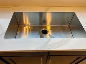 Fregadero bajo encimera sobre mueble oscuro. Fregadero de acero bajo encimera blanca con veta gris, sobre frentes de madera oscura.