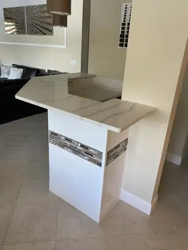 Barra con encimera veteada. Barra con encimera blanca de veta gris sobre frente de pieza blanca en relieve con franja de mosaico.