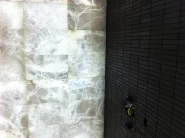 Pared translúcida retroiluminada. Detalle de pared con placas translúcidas retroiluminadas de veta gris junto a un paño de azulejo oscuro con las tomas de grifería.