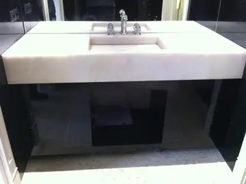Lavabo integrado en encimera blanca. Encimera blanca de canto grueso con lavabo integrado, sobre un mueble negro brillante.