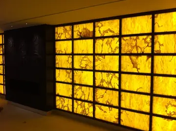 Paramento retroiluminado en tono ámbar. Pared de placas translúcidas en tono ámbar con veta marrón, retroiluminadas y enmarcadas por perfiles oscuros.
