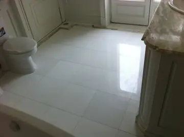 Suelo de baño blanco con cenefa. Pavimento pulido blanco en piezas grandes con cenefa perimetral, junto a un mueble de lavabo con encimera veteada.