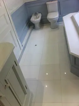 Baño con pavimento blanco y cenefa gris. Pavimento pulido blanco en piezas grandes con cenefa gris a lo largo del zócalo, entre el mueble y la bañera.
