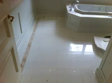 Suelo blanco con cenefa junto a la bañera. Pavimento pulido blanco con cenefa en tono rosado que recorre el baño hasta la bañera.