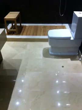Baño con suelo pulido en tono crema. Pavimento pulido en tono crema con veta suave y escalón hacia la ducha con tarima de madera.