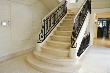 Escalera de peldaños en tono crema. Escalera de peldaños en tono crema con arranque curvo, zanca a juego y barandilla de forja negra.