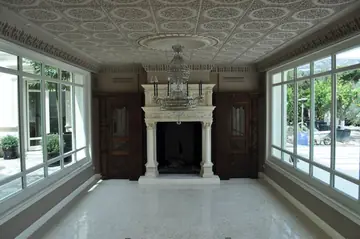 Salón con chimenea y suelo pulido. Salón con pavimento pulido en tono claro y chimenea blanca tallada entre dos ventanales.