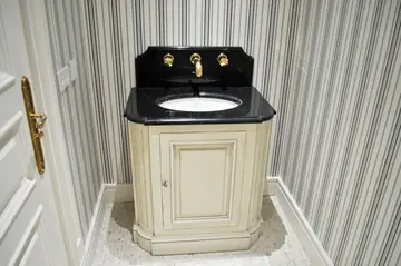 Mueble de lavabo con encimera negra. Mueble de lavabo con encimera y copete negros pulidos, grifería dorada y suelo de pequeñas piezas claras.