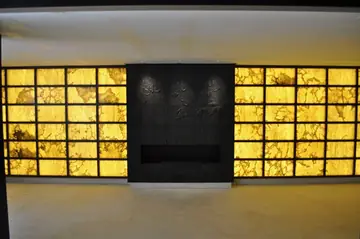 Pared retroiluminada con chimenea. Paramento de placas translúcidas en tono ámbar iluminadas desde dentro, con la chimenea en un panel oscuro central.