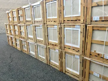 Cajas de baldosas apiladas en el patio. Pared de cajas de madera en tres alturas con baldosas pulidas en tono crema y vetas marcadas.