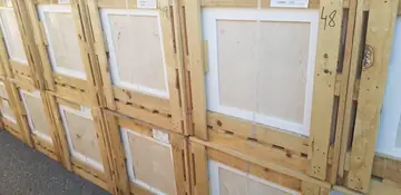 Frente de cajas con baldosas en tono crema. Cajas de madera apiladas con baldosas pulidas en tono crema y vetas visibles tras el poliestireno.