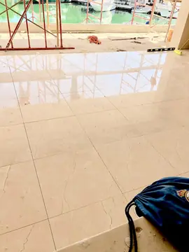 Pavimento pulido con el andamio reflejado. Pavimento de piezas grandes pulidas en tono crema recién colocado, con el andamio reflejado y el agua al fondo.