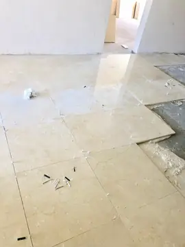 Colocación de pavimento con niveladores. Pavimento de piezas grandes en tono crema durante la colocación, con niveladores en las juntas y la solera a la derecha.