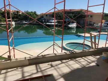 Piscina vista desde la terraza con andamio. Piscina con zona de playa y jacuzzi vista a través del andamio de la terraza en obra.