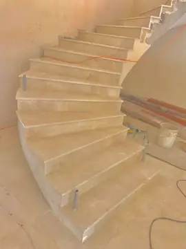 Escalera curva revestida en tono crema. Escalera curva con peldaños y tabicas en tono crema recién colocados, a falta de barandilla.