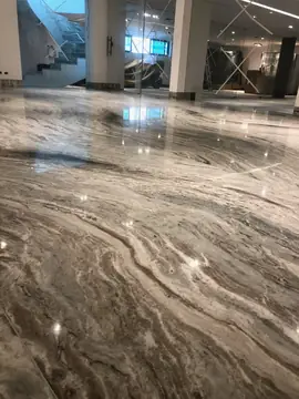 Pavimento pulido con escalera al fondo. Gran superficie de pavimento pulido en gris con vetas onduladas; al fondo, escalera revestida a juego.