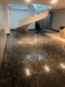 Pavimento oscuro junto a escalera curva. Pavimento pulido oscuro con vetas claras al pie de una escalera helicoidal, todavía con protecciones de obra.