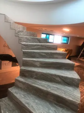 Arranque de escalera con peldaños veteados. Peldaños en gris veteado en el arranque de una escalera curva, con el mobiliario aún tapado alrededor.
