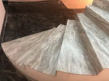 Peldaños de escalera curva desde arriba. Huellas y tabicas en gris veteado de una escalera curva, con la veta visible en el canto de cada peldaño.