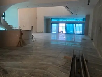 Salón en obra con pavimento colocado. Salón amplio con el pavimento veteado ya colocado, material de obra en primer plano y ventanales todavía protegidos.