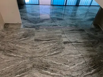 Pavimento de losas con veta marcada. Losas pulidas en gris con vetas horizontales muy marcadas, ante un ventanal todavía protegido con lámina azul.