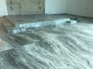 Tarima y escalón con pavimento veteado. Plataforma elevada con peldaño perimetral revestida en gris veteado a juego con el suelo, con cables de obra sueltos.