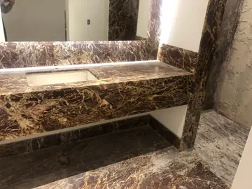 Encimera de lavabo con faldón veteado. Encimera de lavabo con faldón y zócalo en tono granate oscuro con vetas doradas y una línea de luz entre zócalo y encimera.