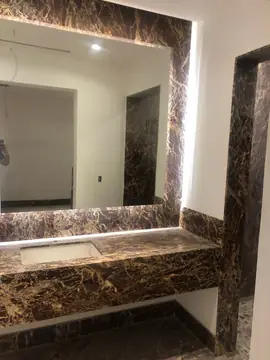 Lavabo con espejo enmarcado veteado. Espejo enmarcado con piezas en tono granate y vetas doradas sobre la encimera del lavabo, con la jamba de la puerta a juego.