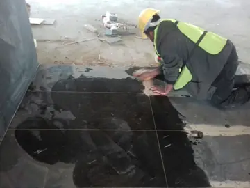 Repaso de juntas en pavimento negro. Un operario repasa con máquina las juntas de un pavimento negro en piezas grandes, con parte de la superficie mojada.