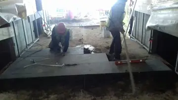 Colocación de piezas oscuras en vestíbulo. Un operario ajusta piezas oscuras recién asentadas mientras otro trabaja de pie junto al tramo colocado, con un nivel sobre el suelo.