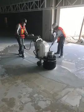 Pulido del pavimento en obra. Dos operarios con mascarilla pulen el pavimento con una pulidora de suelos.