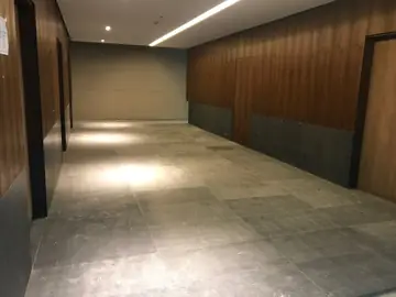 Pasillo con pavimento gris de gran formato. Pasillo con pavimento gris en piezas grandes, zócalo oscuro y paneles en tono madera.
