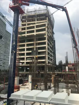 Torre en estructura y bomba de hormigón. Torre de hormigón en construcción con la pluma de la bomba de hormigón y armaduras de pilares en primer término.