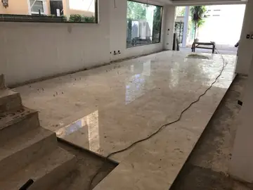 Pavimento pulido a medio colocar en el salón. Gran superficie de piezas pulidas en tono crema ya asentadas, con la franja perimetral y la escalera aún pendientes.