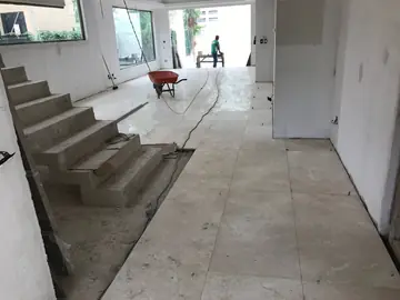 Pavimento colocado junto a la escalera de obra. Piezas en tono crema asentadas hasta el arranque de la escalera, aún sin revestir, con la franja inferior por completar.