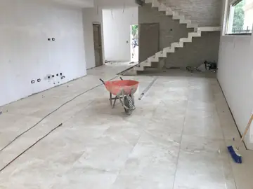 Salón con el pavimento recién colocado. Superficie de piezas en tono crema ya asentada, con la escalera volada al fondo todavía sin revestir.