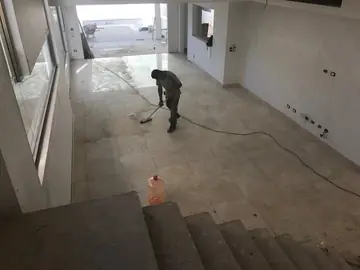 Limpieza del pavimento recién colocado. Un operario friega la superficie de piezas en tono crema del salón, vista desde lo alto de la escalera.