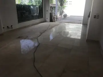 Salón con pavimento pulido en tono crema. Piezas con brillo en parte de la superficie y el cableado de la obra aún por retirar.