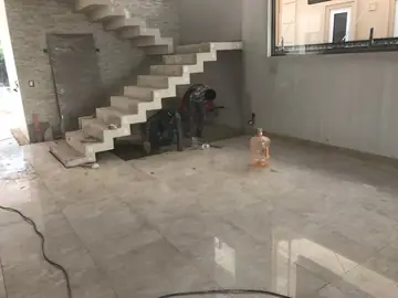 Salón con pavimento y escalera en obra. Pavimento pulido en tono crema ya colocado mientras dos operarios trabajan bajo la escalera volada, aún sin revestir.