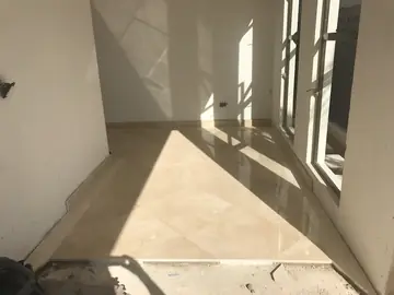 Estancia con pavimento en diagonal. Piezas pulidas en tono crema colocadas en diagonal, con rodapié perimetral y luz de las puertas acristaladas.