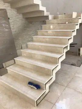 Escalera revestida en tono crema. Huellas y tabicas en piezas pulidas en tono crema, con ranuras antideslizantes en los peldaños inferiores y los laterales aún sin rematar.