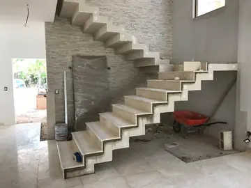 Revestimiento de escalera volada en tono crema. Tramo inferior de la escalera ya revestido en tono crema, con el tramo superior aún en hormigón.