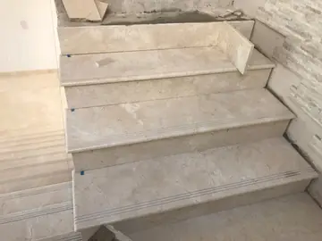 Peldaños revestidos junto a la meseta. Peldaños en piezas pulidas en tono crema con ranuras antideslizantes y la pared de plaqueta en tiras al lado.