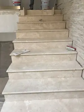 Tramo de escalera durante el revestimiento. Huellas y tabicas en tono crema ya colocadas, con una herramienta sobre un peldaño y el superior aún por rematar.