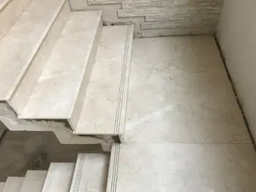 Meseta de escalera revestida en tono crema. Meseta amplia en piezas pulidas con veta y peldaños con ranuras antideslizantes, vista desde arriba.